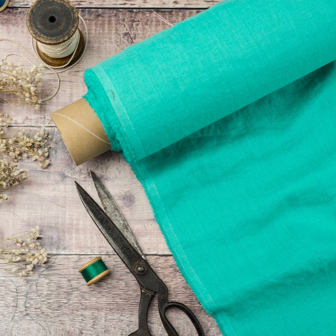 Aqua linen fabric, ready to cut, with scissors, thread bobbins and flowers