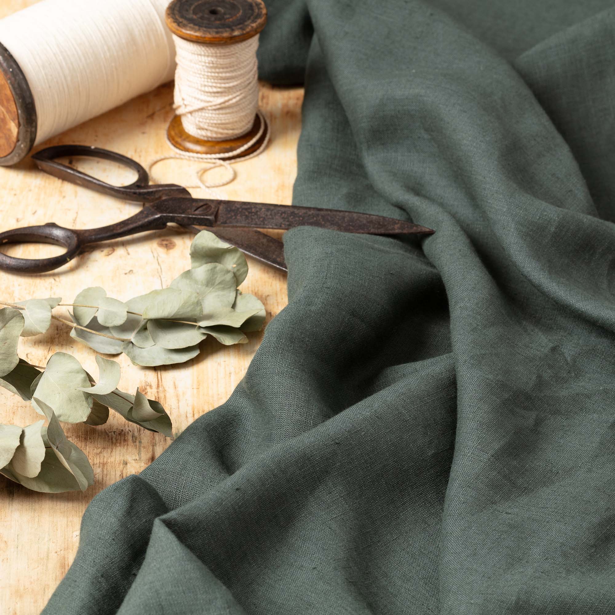Dark Slate Green linen fabric, ready to cut, with scissors, thread bobbins and dried eucalyptus