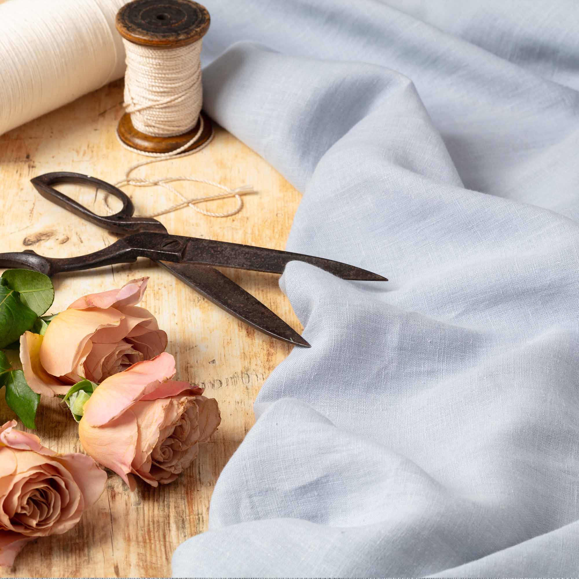 Dove Blue linen fabric, ready to cut, with scissors, thread bobbins and flowers