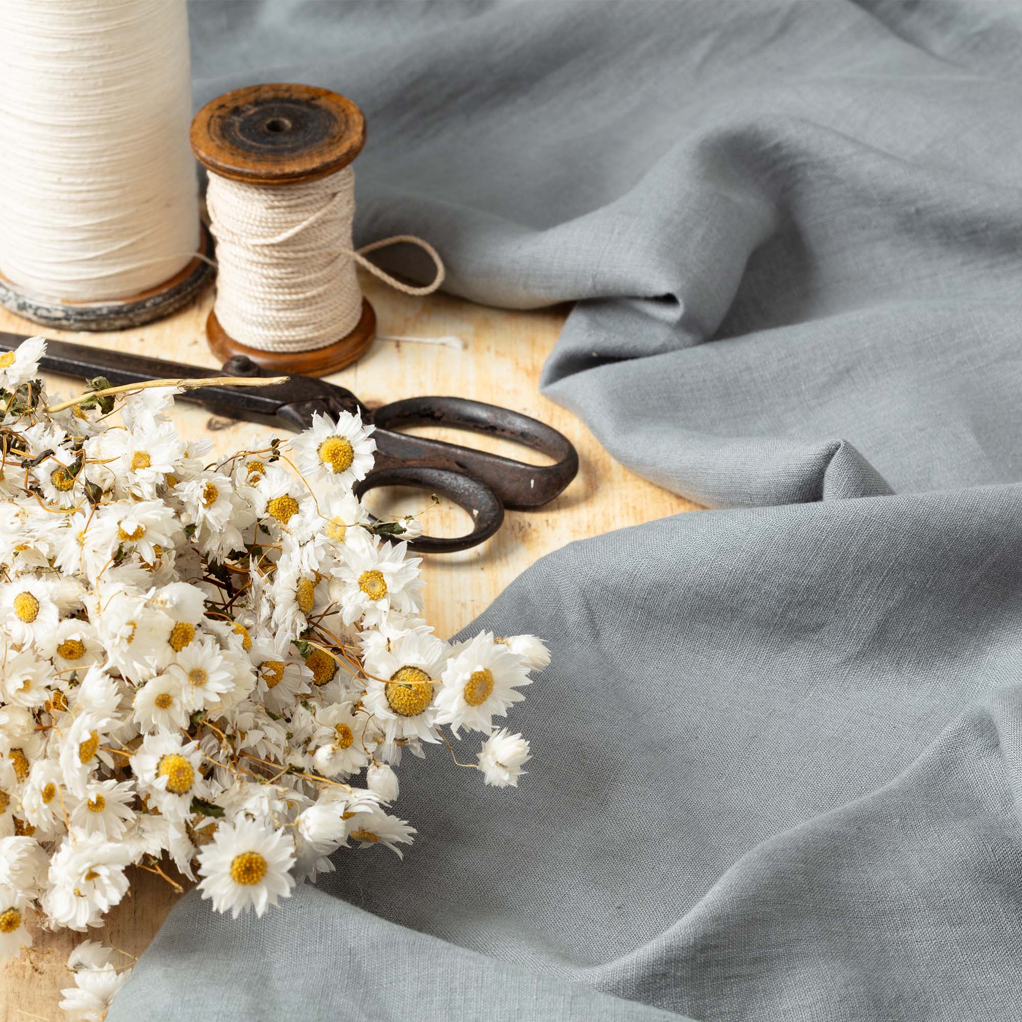 Grey linen fabric, ready to cut, with scissors, thread bobbins and flowers