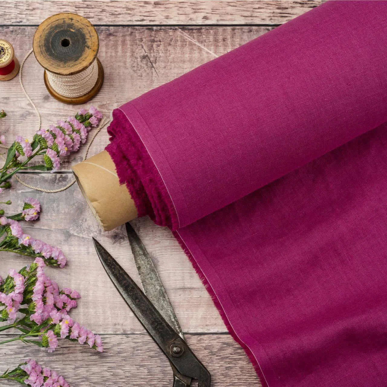 Magenta linen fabric, ready to cut, with scissors, thread bobbins and flowers
