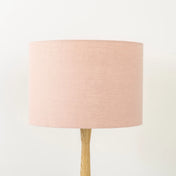 A blush pink linen lampshade on a wooden lamp base, with a textured weave design, photographed against a white background.