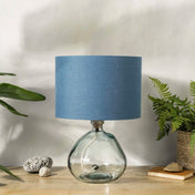 Blue linen lampshade with recycled glass base on wooden desk with plants