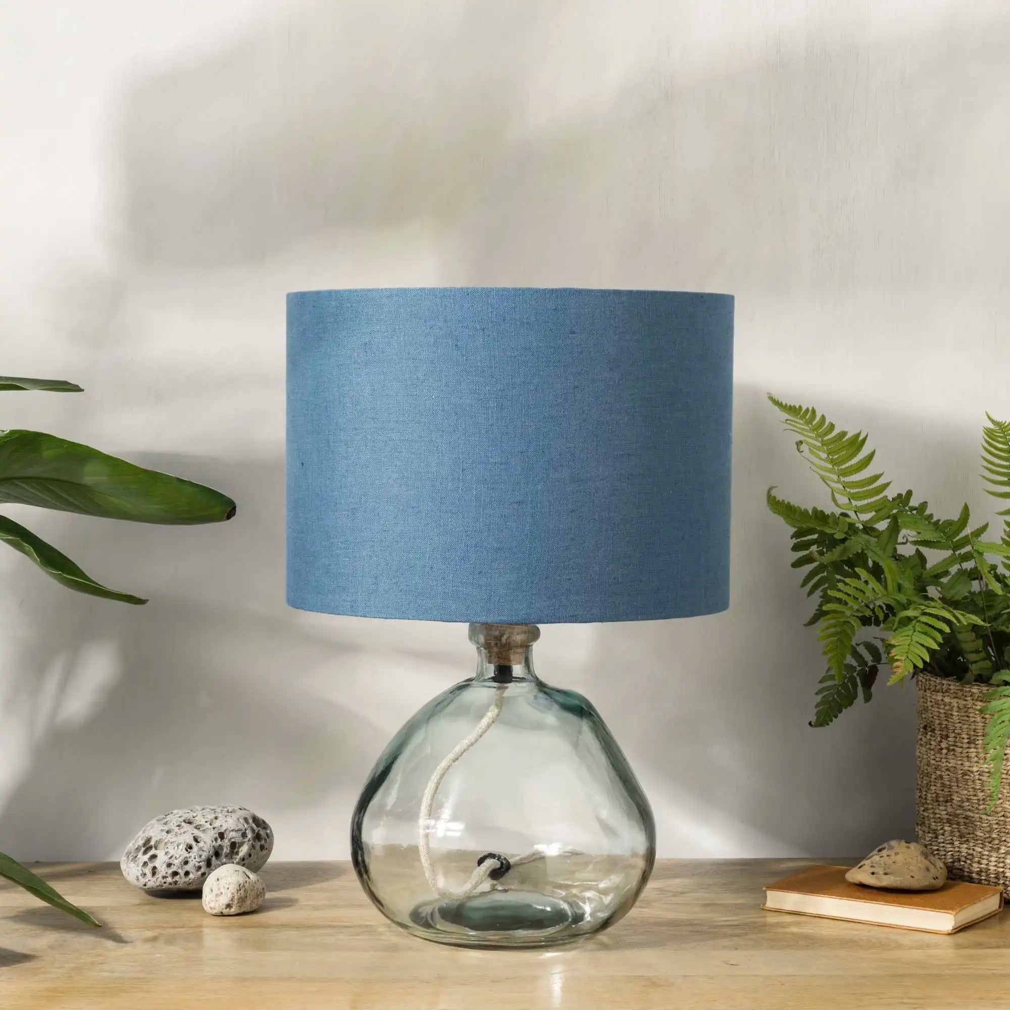 Blue linen lampshade with recycled glass base on wooden desk with plants