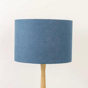 A dusty blue linen lampshade on a wooden lamp base, with a textured weave design, photographed against a white background.