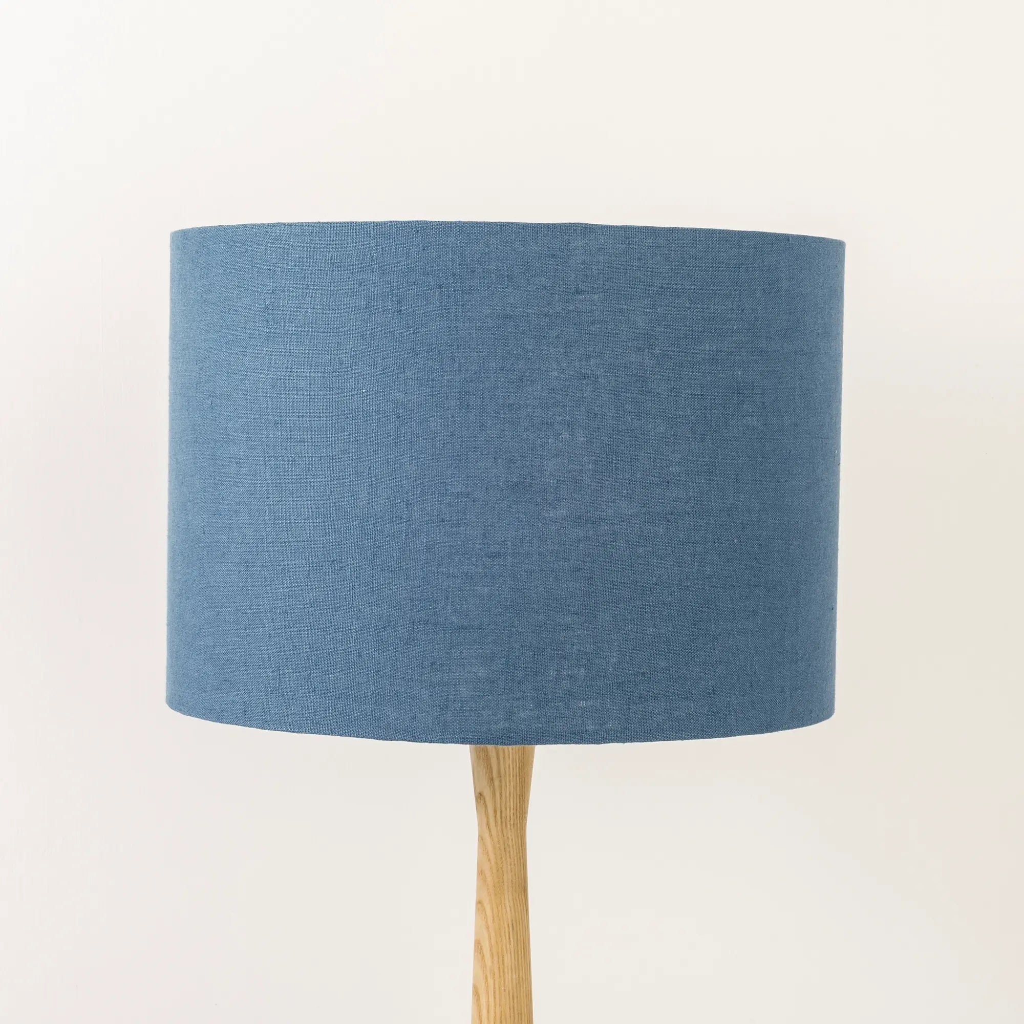 A dusty blue linen lampshade on a wooden lamp base, with a textured weave design, photographed against a white background.