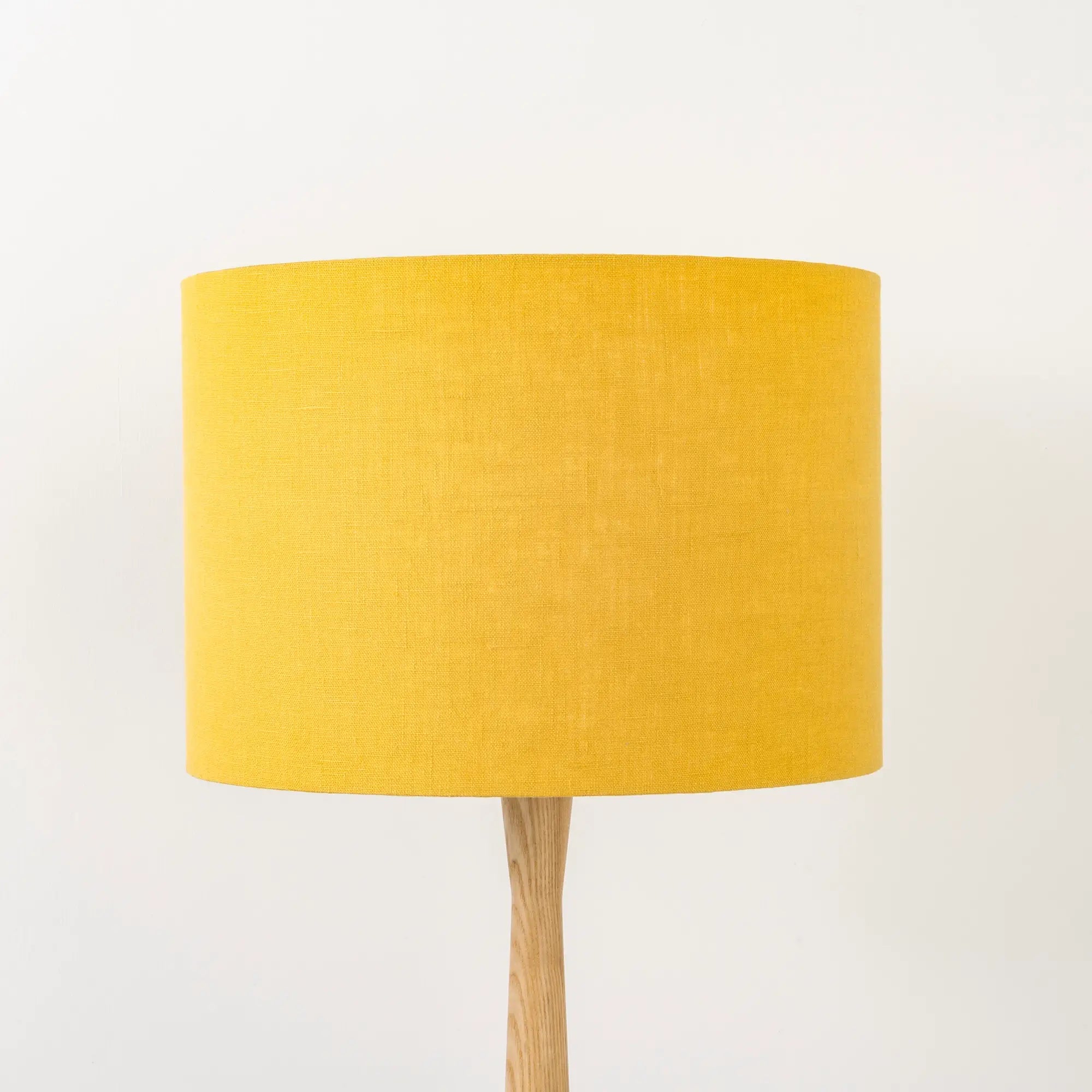 A honey yellow linen lampshade on a wooden lamp base, with a textured weave design, photographed against a white background.