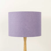 A lavender linen lampshade on a wooden lamp base, with a textured weave design, photographed against a white background.