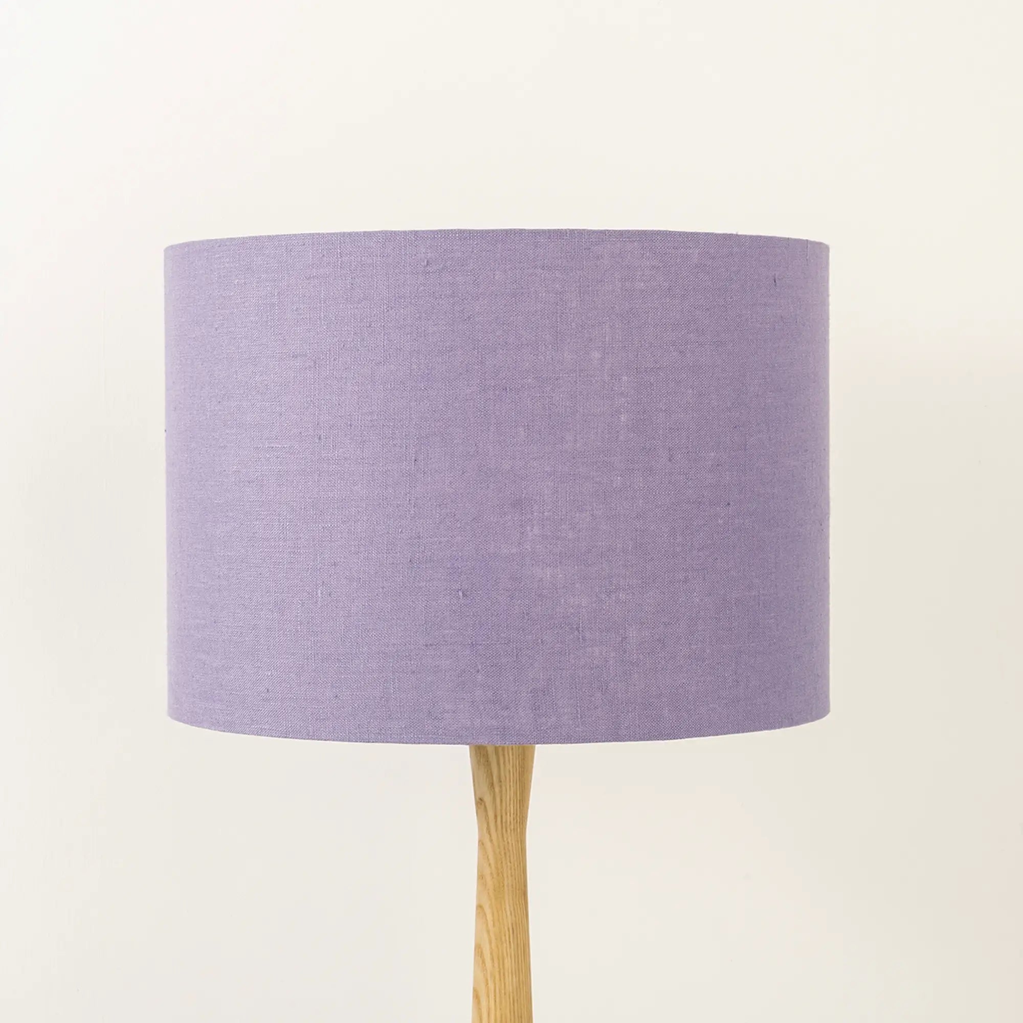 A lavender linen lampshade on a wooden lamp base, with a textured weave design, photographed against a white background.