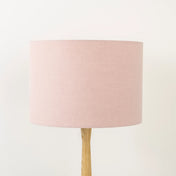 A dusty pink linen lampshade on a wooden lamp base, with a textured weave design, photographed against a white background.