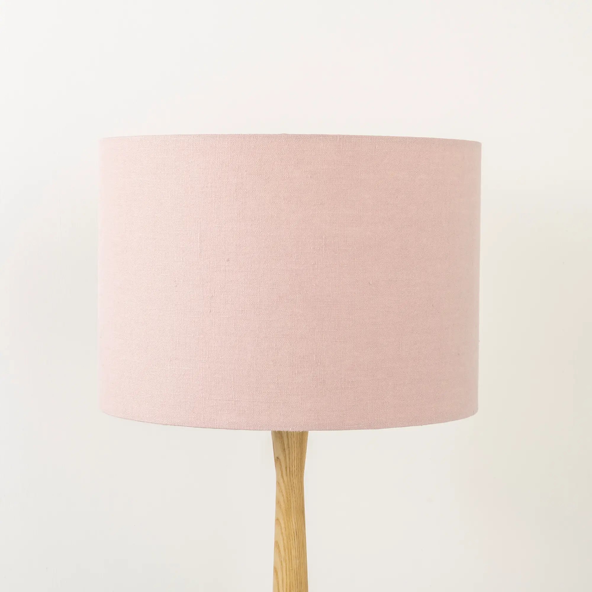 A dusty pink linen lampshade on a wooden lamp base, with a textured weave design, photographed against a white background.