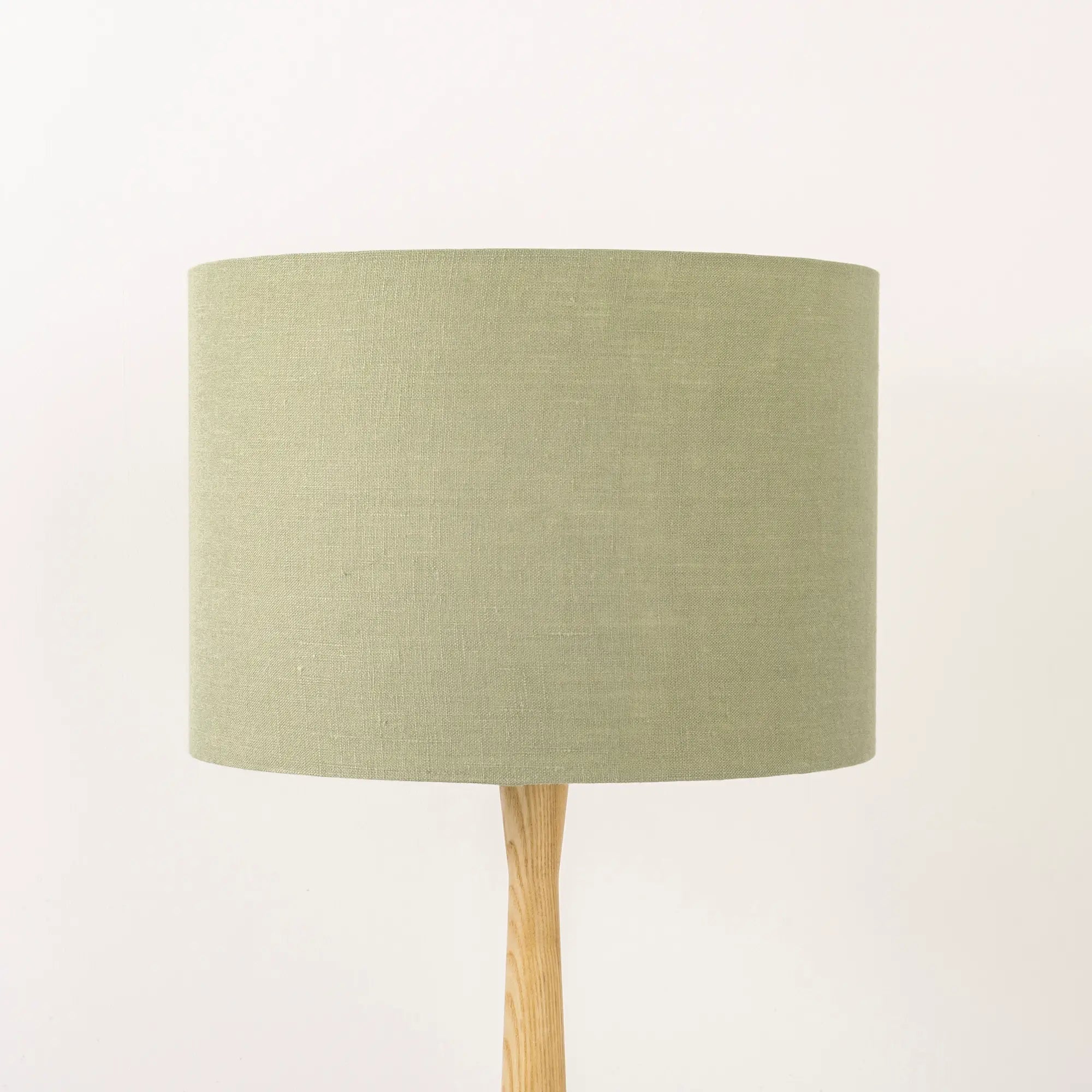A light sage green lampshade on a wooden lamp base, with a textured weave design, photographed against a white background.