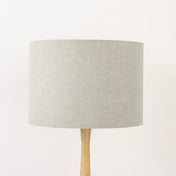 A beige natural linen lampshade on a wooden lamp base, with a textured weave design, photographed against a white background.
