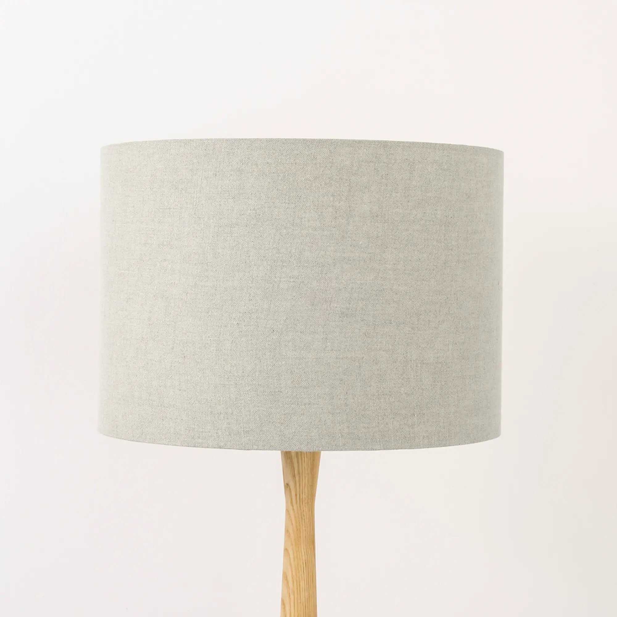 A beige natural linen lampshade on a wooden lamp base, with a textured weave design, photographed against a white background.