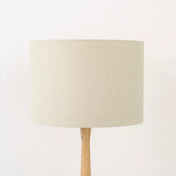 An oatmeal linen lampshade on a wooden lamp base, with a textured weave design, photographed against a white background.