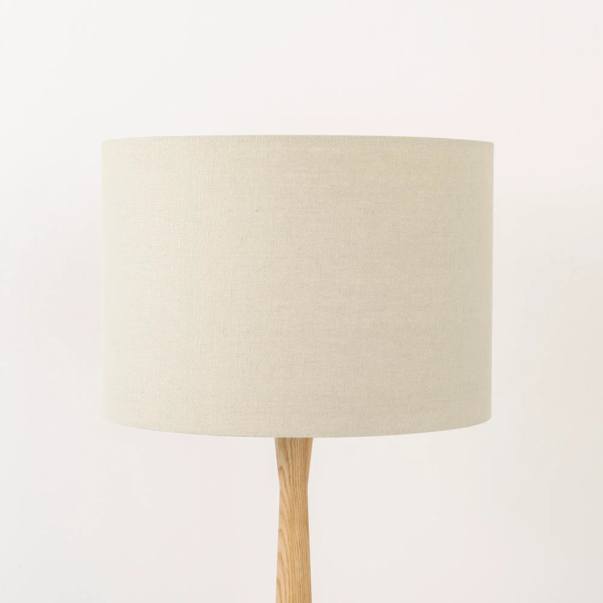 An oatmeal linen lampshade on a wooden lamp base, with a textured weave design, photographed against a white background.