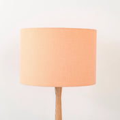 A peach lampshade on a wooden lamp base, with a textured weave design, photographed against a white background.