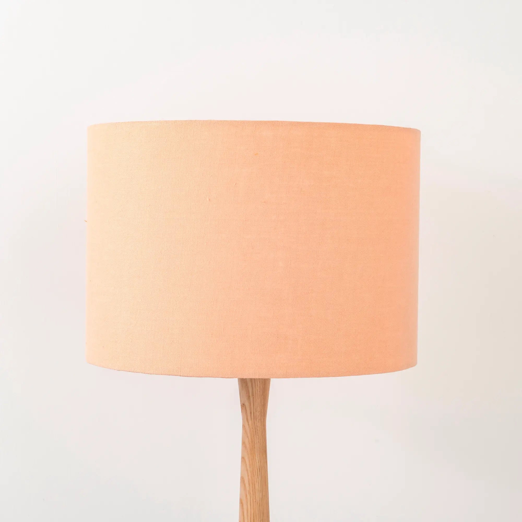 A peach lampshade on a wooden lamp base, with a textured weave design, photographed against a white background.