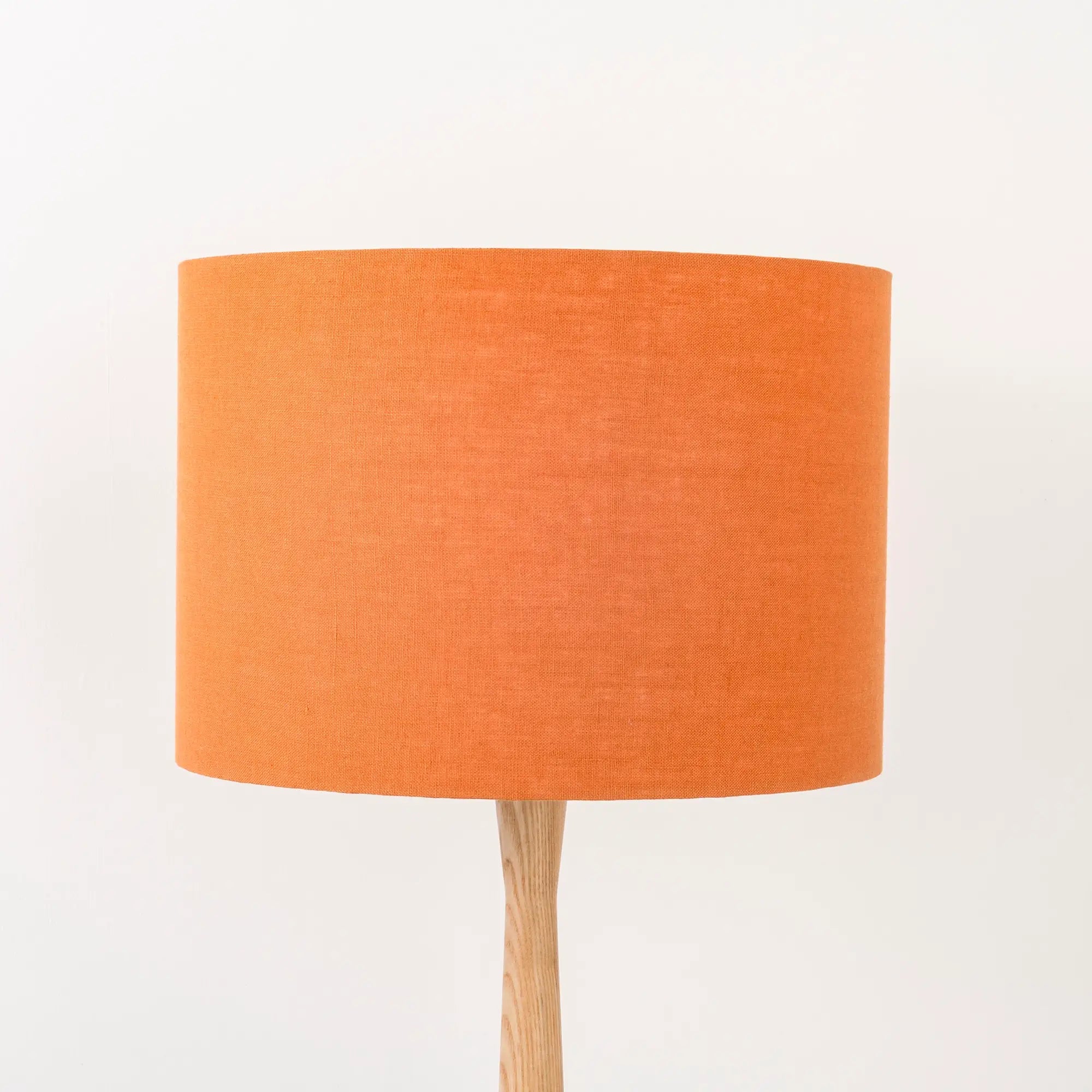 A pumpkin orange linen lampshade on a wooden lamp base, with a textured weave design, photographed against a white background.