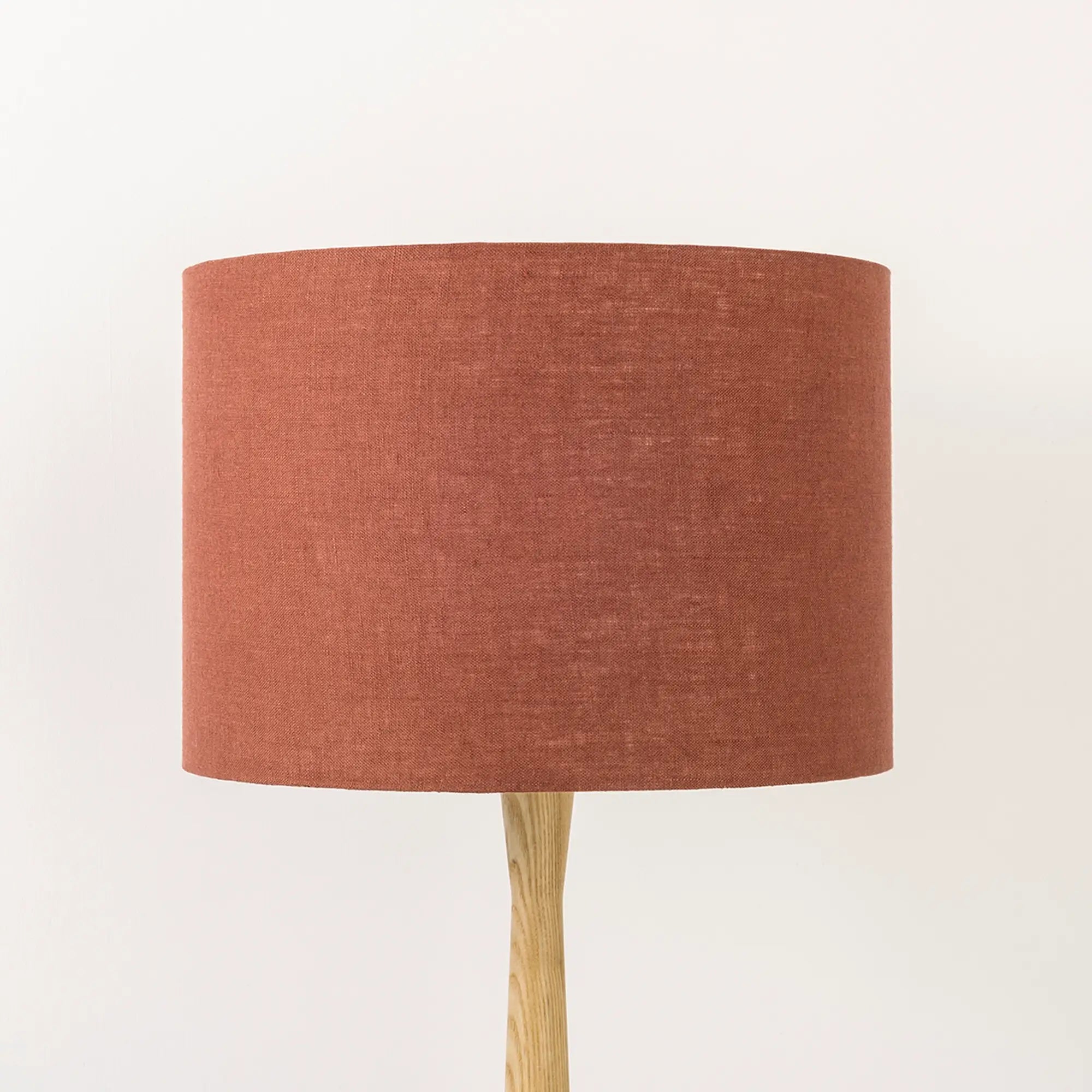 A terracotta lampshade on a wooden lamp base, with a textured weave design, photographed against a white background.
