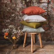 Stack of washed linen cushion covers on wooden stool with dried flowers
